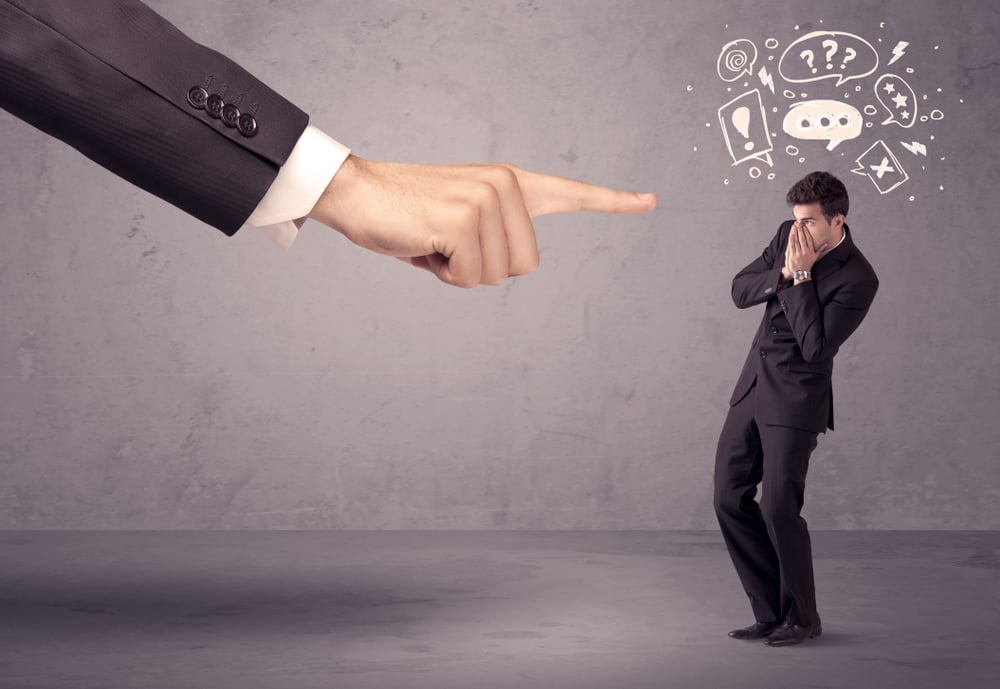 A young confused businessman being fired by large boss hand concept with drawn speech bubbles, exlamation, question marks