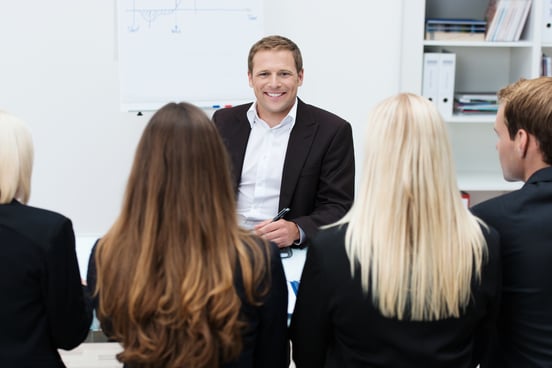 Confident businessman or team leading in a meeting sitting at his desk facing his colleagues with a pleased smile on his face-1