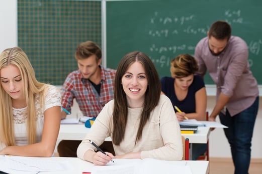 Pretty young female college student sitting at her desk working in the classroom with her peers