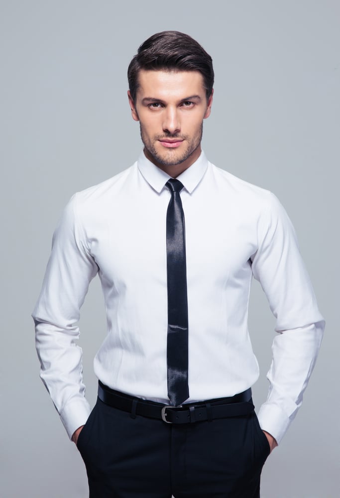 Young businessman standing with hands in pocket over gray background